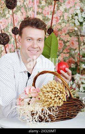 L'homme est assis à table avec un beau panier avec une gerbe de blé et tient des fruits dans un intérieur rétro. Banque D'Images