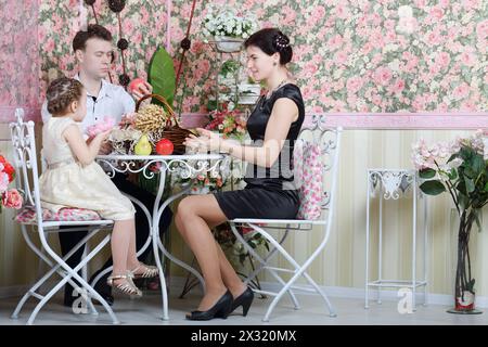 Père, mère et fille assis à table avec des fruits, et beau panier à l'intérieur rétro. Banque D'Images