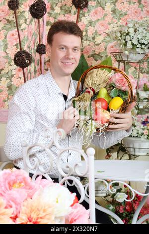 L'homme est assis à table et tient le panier avec la gerbe de blé et les fruits dans l'intérieur rétro. Banque D'Images