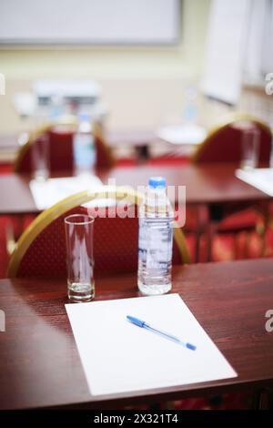 Table avec bouteille, verre, drap et stylo et chaises rouges dans la salle pour les formations d'affaires. Banque D'Images