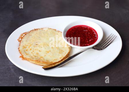 Crêpes à la confiture de framboises sur une assiette avec une fourchette sur une table en bois brun Banque D'Images