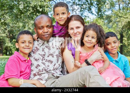 Grande famille interraciale de six se trouve serré embrassé dans l'herbe sur la pelouse dans le parc Banque D'Images