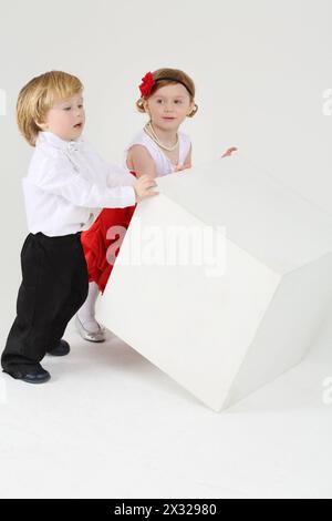 Petit garçon et jolie fille retournent grand cube blanc sur fond blanc. Banque D'Images