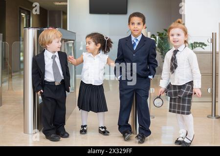 Quatre enfants vêtus de vêtements d'affaires près de la barrière du centre d'affaires, une fille tenant une loupe Banque D'Images