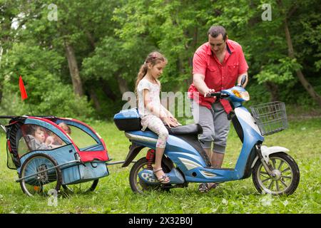 Père et trois enfants sur un scooter avec chariot sur la nature Banque D'Images