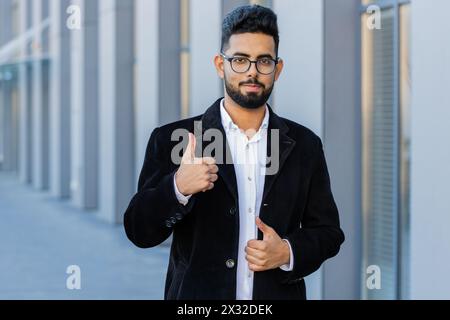 J'aime. Heureux homme d'affaires indien soulève les pouces vers le haut accepte donne une réponse positive recommande la publicité aime la rétroaction de bonne idée, célébrant la victoire de succès. Arabian Hindu freelance gars dans la rue de la ville Banque D'Images