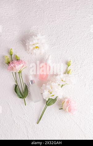 Deux flacons cosmétiques mats avec une pipette avec un produit d'auto-soin naturel sur un fond clair avec des fleurs d'austome. Vue de dessus verticale Banque D'Images