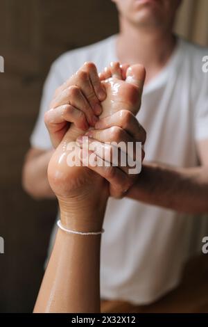 Plan vertical recadré d'un masseur mâle méconnaissable faisant masser le talon d'une cliente, pressant les points d'acupuncture du pied avec les doigts Banque D'Images