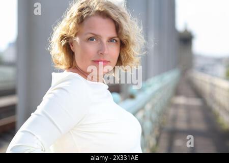 Heureuse belle femme blonde en robe blanche se tient sur le pont. Banque D'Images