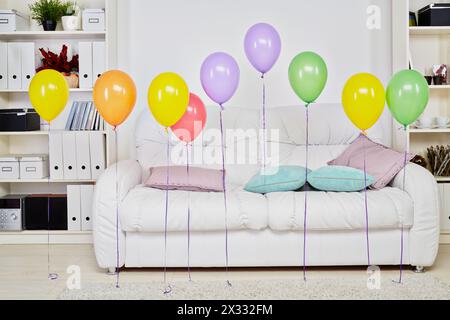 Intérieur de la chambre avec grand canapé blanc doux, tapis léger sur le sol et ballons de rangée suspendus dans l'air Banque D'Images