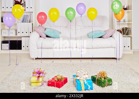 Chambre avec grand canapé, coffrets cadeaux sur le sol et ballons d'anniversaire suspendus dans l'air Banque D'Images