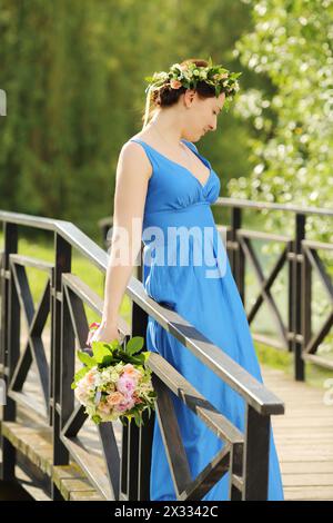 Belle femme rêveuse en robe bleue avec des stands de bouquet sur le pont dans le parc. Banque D'Images