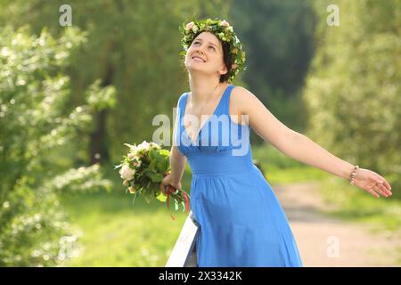 Belle femme souriante en robe bleue avec bouquet représente oiseau dans le parc. Banque D'Images