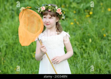 Petite fille drôle en blanc regarde le papillon assis au filet sur la prairie verte. Banque D'Images