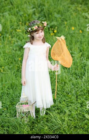 Petite fille dans les stands blancs avec filet papillon et coop sur la prairie verte. Banque D'Images