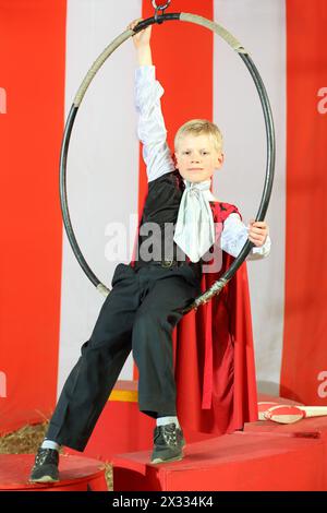 Portrait de petit garçon en costume noir et manteau rouge sur l'anneau de cirque aérien Banque D'Images