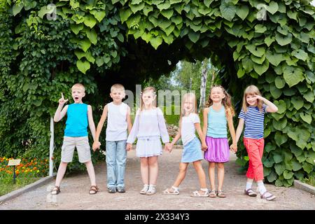 Les enfants se tiennent la main avec le dos au tunnel fait de plantes vertes et de feuilles Banque D'Images