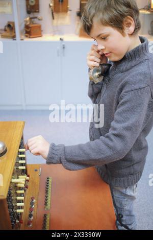 Garçon avec combiné se tient à propos de vieux commutateur téléphonique dans le musée Banque D'Images