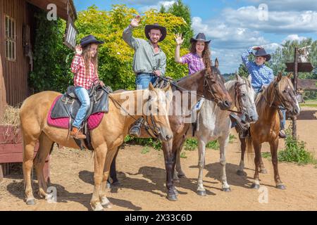 famille de cow-boys de quatre sur des chevaux agitant leurs mains Banque D'Images