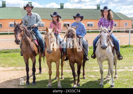 famille de cow-boy de quatre sur des chevaux sur fond de paddock Banque D'Images