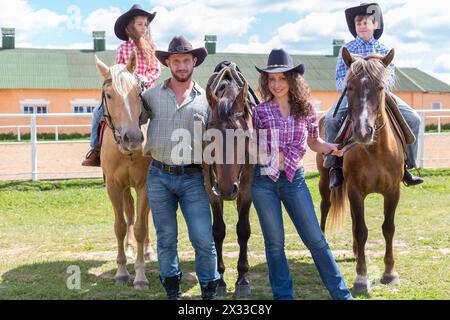 famille de cow-boy de quatre avec des chevaux sur fond de paddock Banque D'Images