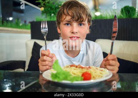 garçon avec un couteau et une fourchette devant une assiette de pâtes Banque D'Images