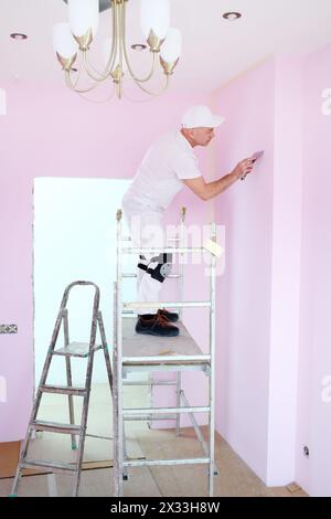 Homme à la truelle à la main debout sur un échafaudage dans une chambre rose Banque D'Images