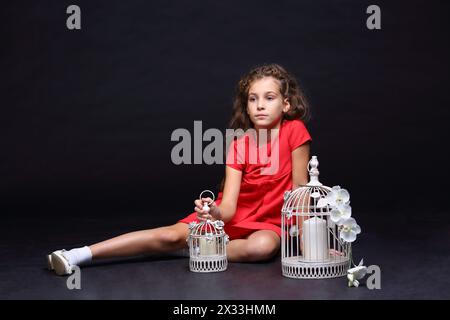 Belle fille en robe rouge assise sur le sol avec deux bougies blanches dans les cellules Banque D'Images