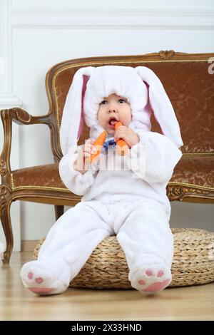 Petit garçon en costume lapin assis sur pouf avec carotte Banque D'Images