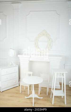 Chambre blanche intérieure avec colonnes de style ancien, cheminée et cadre ajouré, table ronde et chaises, commode et lampe Banque D'Images