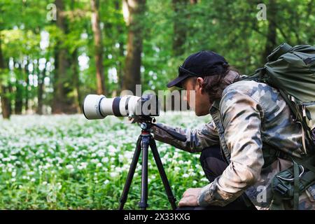 Photographe animalier règle l'appareil photo sur un trépied. L'homme photographie dans la forêt printanière Banque D'Images