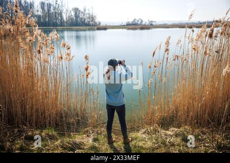 Observation des oiseaux dans la nature. Femme avec des jumelles observant les oiseaux et les animaux au lac Banque D'Images