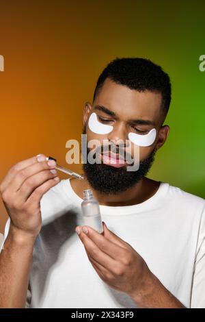 Beau jeune homme appliquant des patchs oculaires pour sa routine de soins de la peau. Banque D'Images