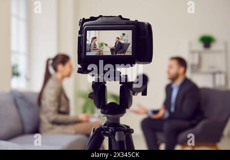 Caméra sur trépied au premier plan, homme d'affaires donnant une interview au journaliste au bureau, journaliste femme Banque D'Images