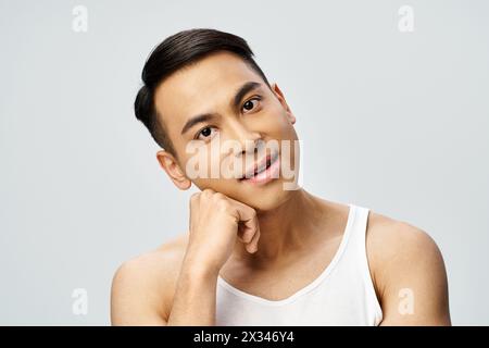 Un bel homme asiatique dans un studio gris frappant une pose tout en portant un débardeur. Banque D'Images