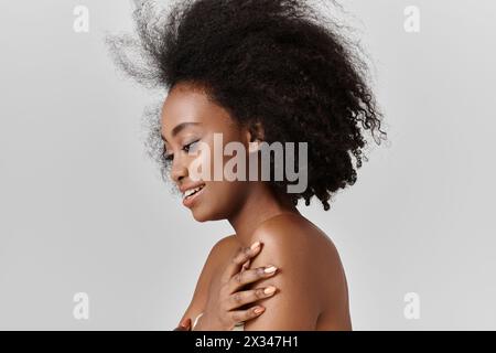 Une jeune femme afro-américaine avec un afro sourit chaleureusement dans un décor de studio. Banque D'Images