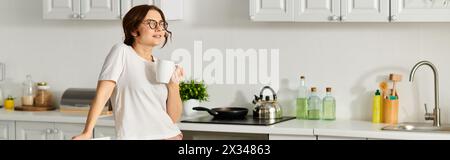 Femme d'âge moyen appréciant une tasse de café dans sa cuisine. Banque D'Images