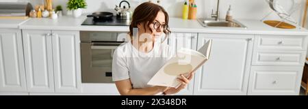 Une femme d'âge moyen englouti dans un livre alors qu'elle était assise dans une cuisine confortable. Banque D'Images