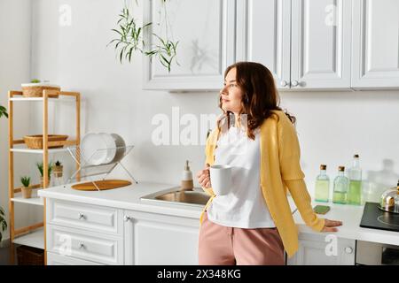 Femme d'âge moyen se tenant calmement dans la cuisine, tenant la tasse. Banque D'Images