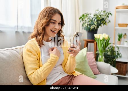 Femme assise sur un canapé engrossée dans son téléphone portable. Banque D'Images