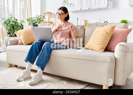 Une femme dans des vêtements de maison confortables est assise sur un canapé, absorbée dans son ordinateur portable. Banque D'Images