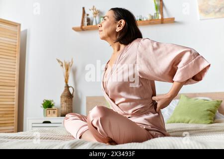 Une femme dans des vêtements de maison confortables est assise sur un lit avec ses mains sur ses hanches. Banque D'Images