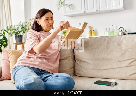 Une femme dans des vêtements de maison confortables est assise sur un canapé, engrossée dans un livre. Banque D'Images