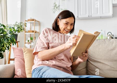 Une femme mature et attrayante dans les vêtements de maison, perdue dans les pages d'un livre alors qu'elle était assise sur un canapé confortable. Banque D'Images