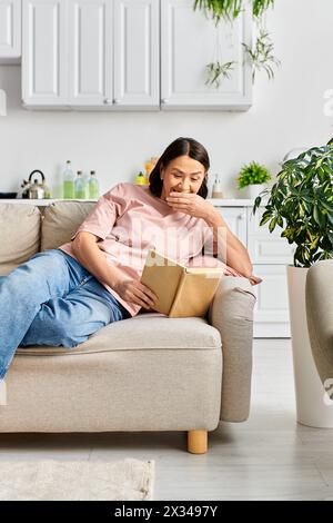 Femme dans des vêtements confortables assis sur un canapé, profondément engrossé dans la lecture d'un livre. Banque D'Images