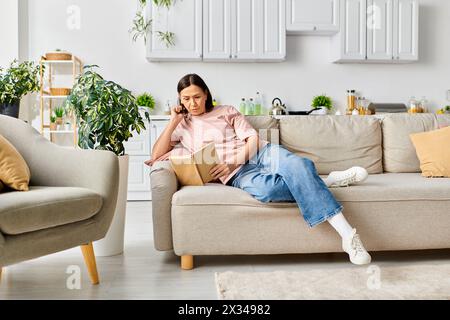 Une femme dans des vêtements confortables assis sur un canapé, engrossée dans un livre de lecture. Banque D'Images