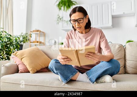 Une femme mature dans des vêtements confortables assis sur un canapé, engrossé dans la lecture d'un livre. Banque D'Images