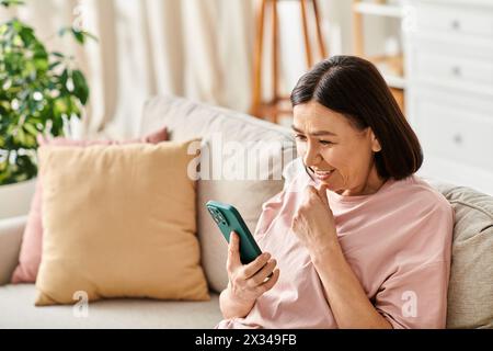 Une femme en tenue confortable englouti dans son téléphone alors qu'elle était assise sur un canapé. Banque D'Images