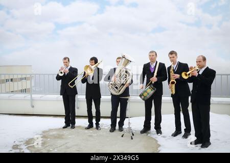 Brass band de six musiciens en costumes jouent sur le toit d'un grand bâtiment à l'hiver Banque D'Images