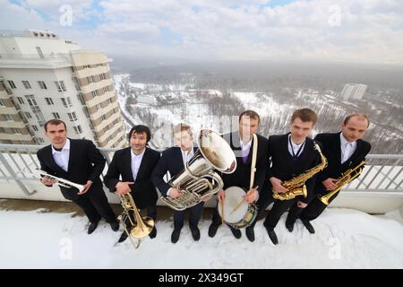 Bande de cuivre de six musiciens en costumes sourire sur le toit d'un grand bâtiment à l'hiver Banque D'Images